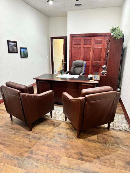 Office with a large dark desk, two brown leather chairs, and a wooden cabinet. A closed wooden door is in the background.