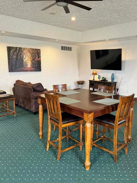 A living room with a dining table, chairs, a sofa, and a TV mounted on the wall.
