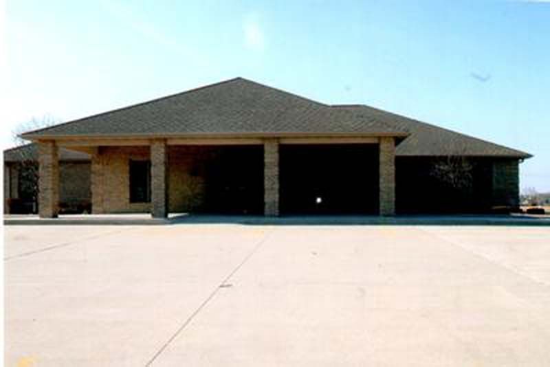 Tan brick building with a large covered entrance supported by dark columns under a dark roof.