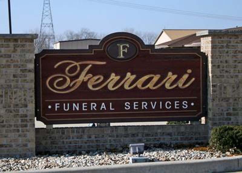 Sign for Ferrari Funeral Services; brown and gold lettering on a brick wall.