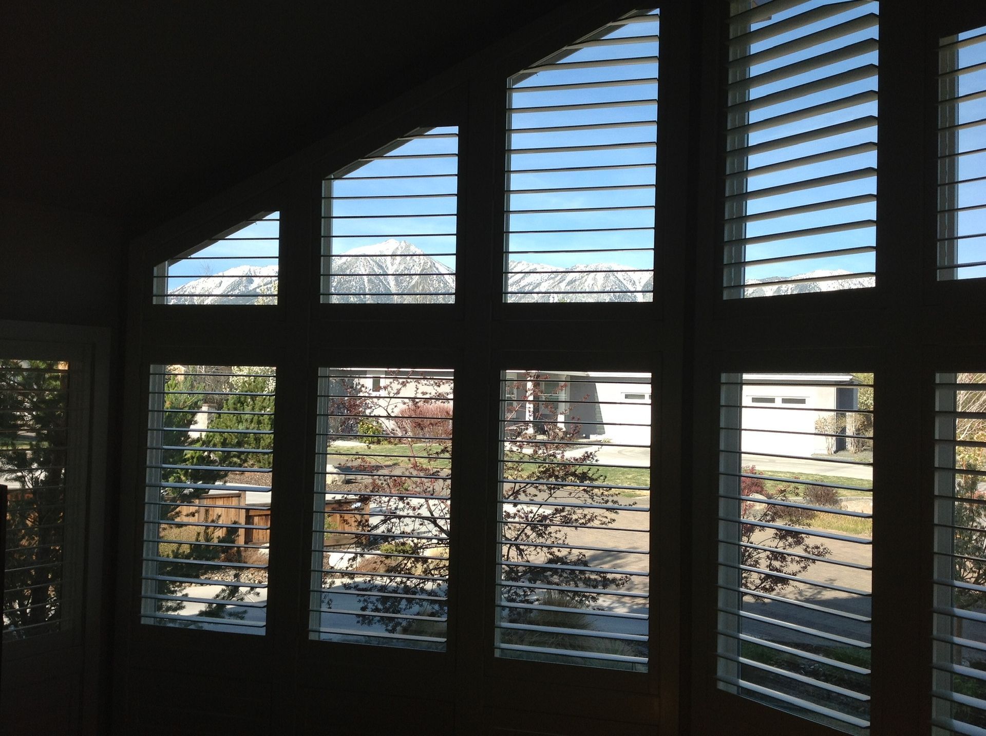 Sunlit window with blinds, showing a suburban street and houses outside