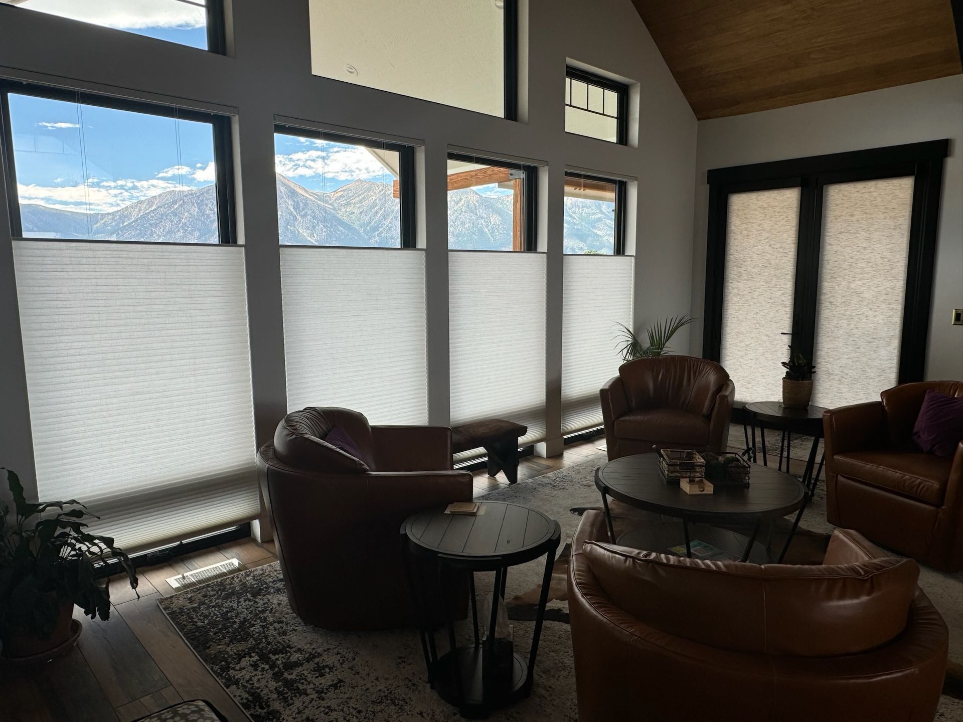 Modern living room with leather chairs, round tables, frosted windows, and mountain view through upper panes