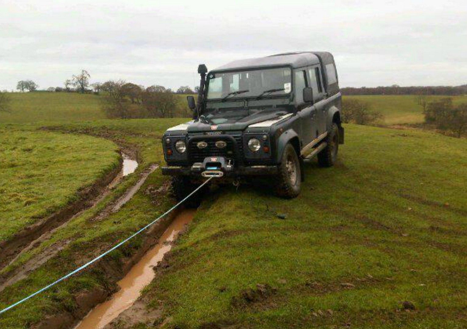 a black 4X4 is stuck in a muddy field with a winch attached to it .