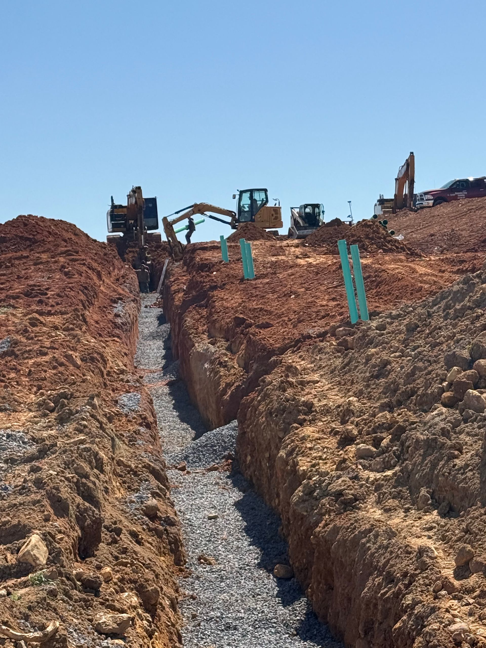 A yellow excavator is pouring gravel into a hole in the ground.