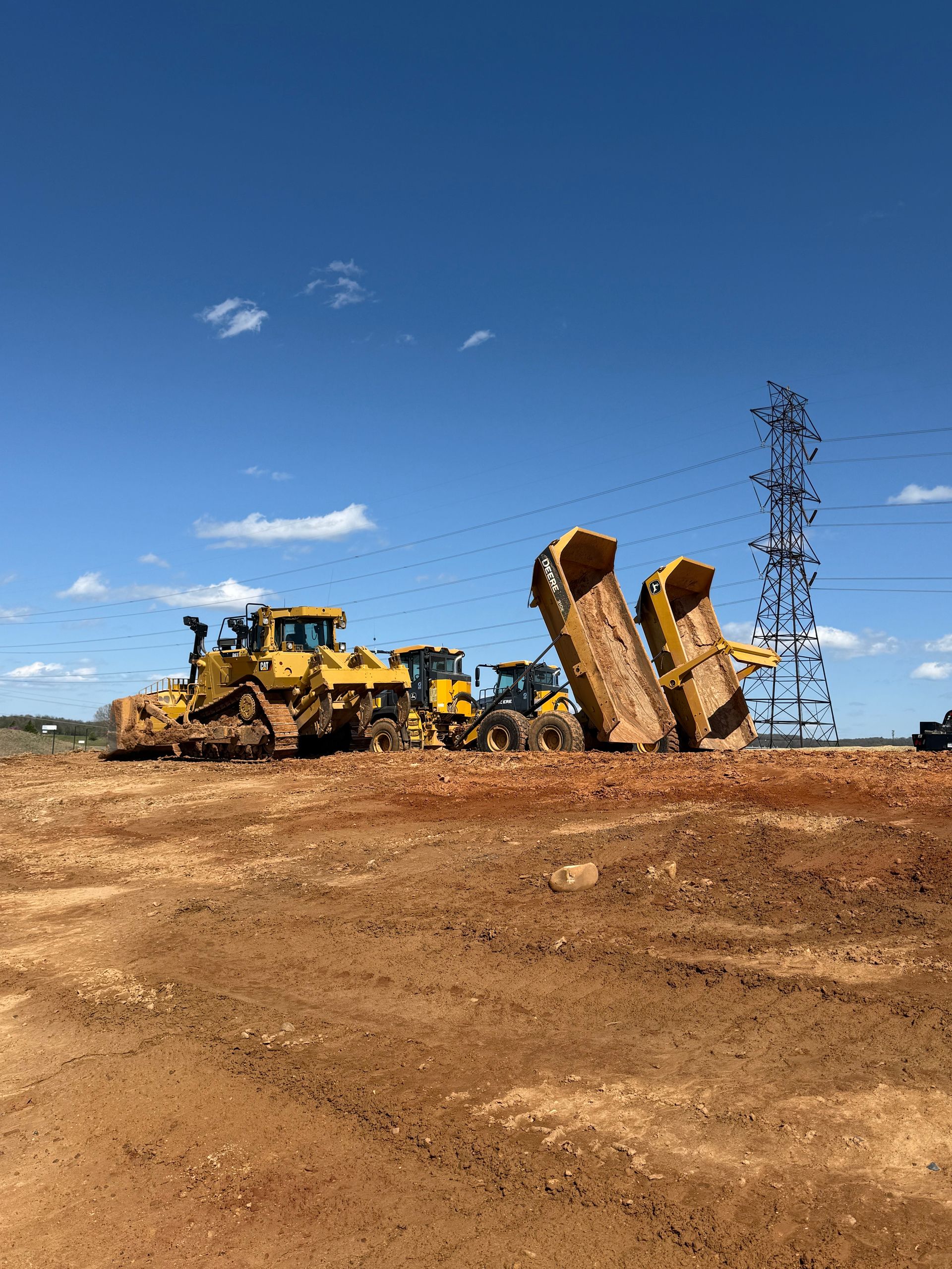 A man is driving a yellow excavator on a dirt road.