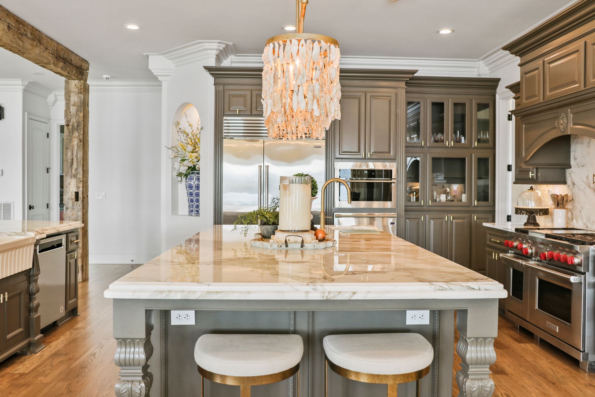 A kitchen with a large island and stools and a chandelier hanging from the ceiling.