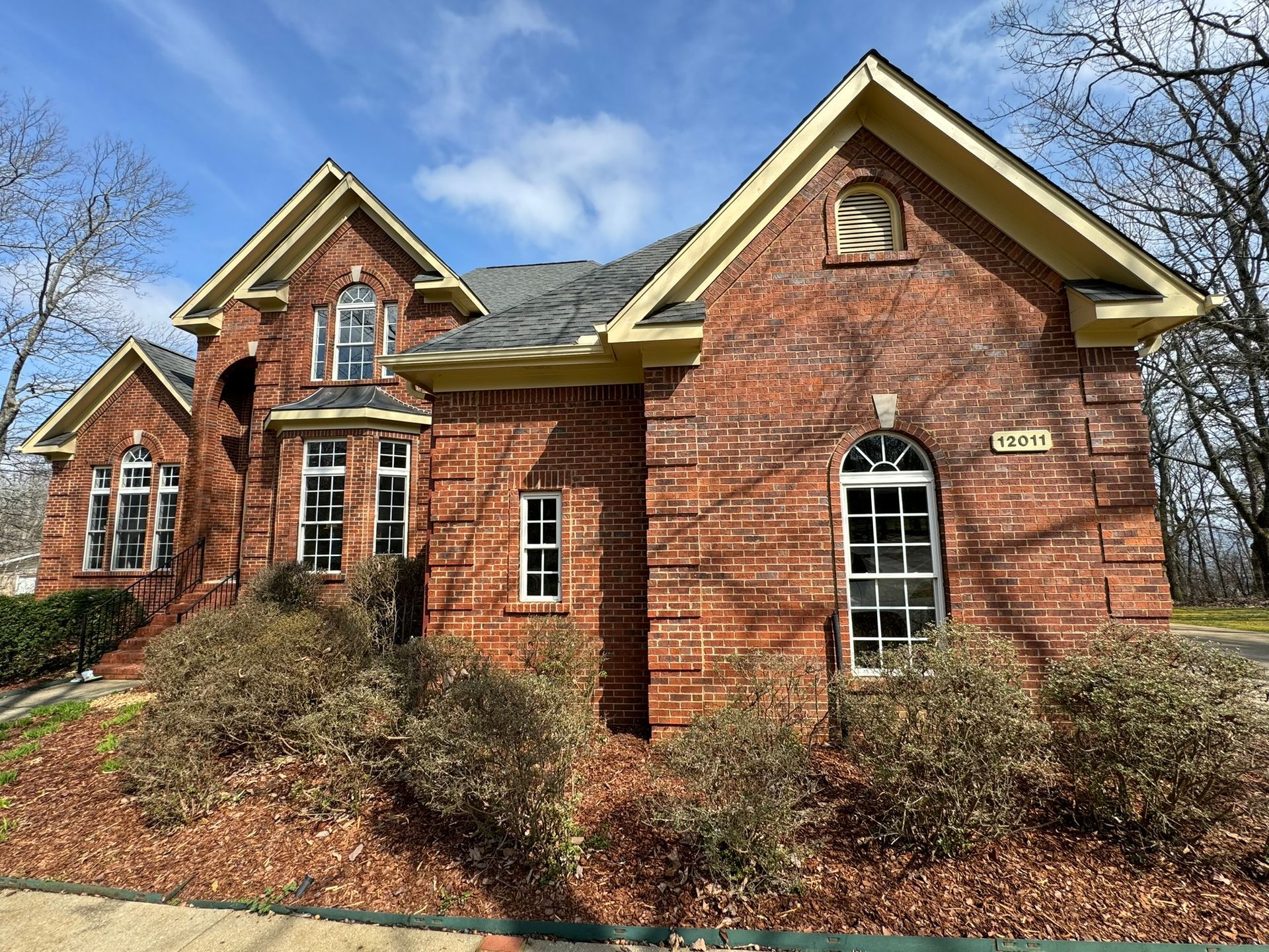A large brick house with a lot of windows and bushes in front of it.