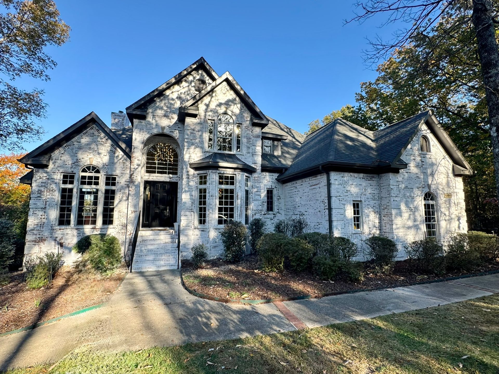 A large white brick house with a black roof is surrounded by trees.
