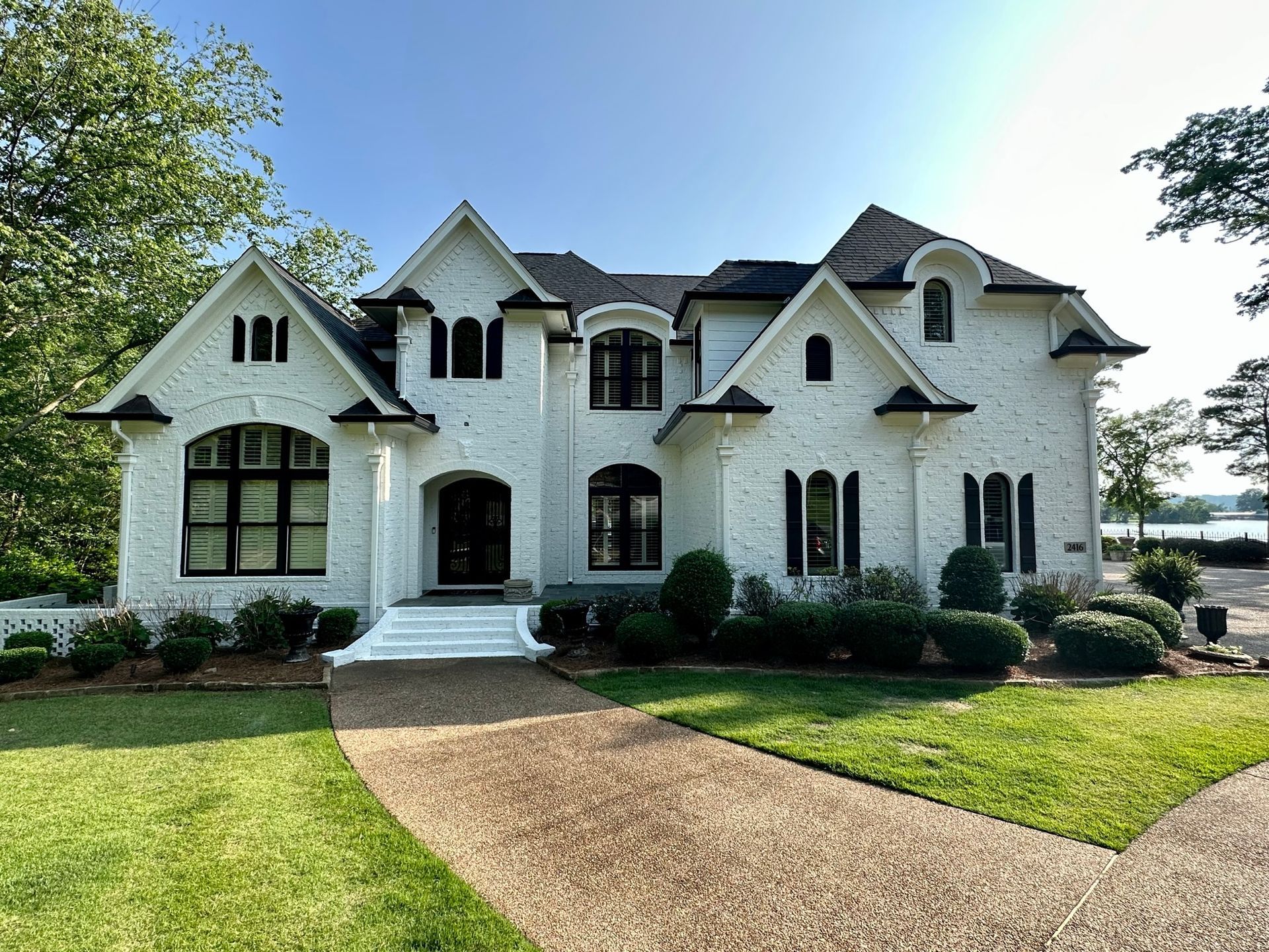 A large white house  lime washed with black trim is sitting on top of a lush green lawn.