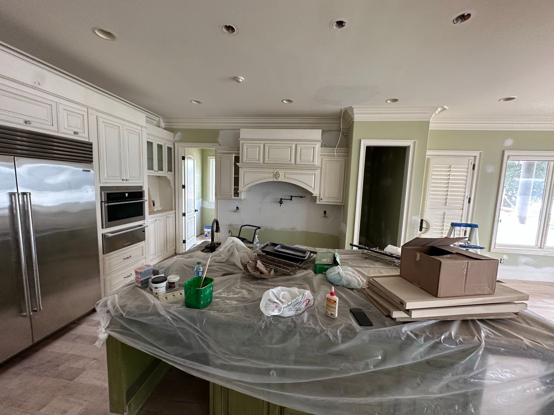 A kitchen is being painted and the island is covered in plastic.