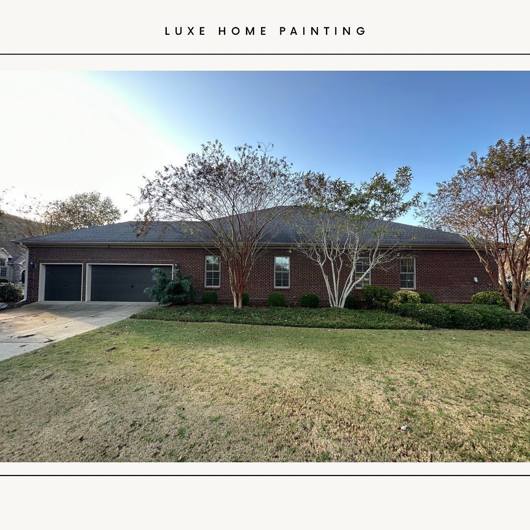 A brick house with a black garage door and a large lawn in front of it.
