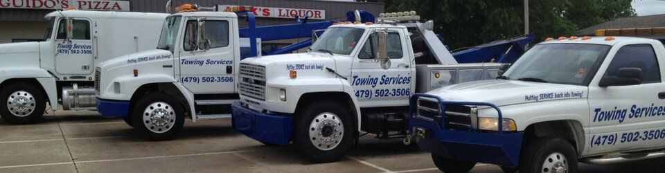 White tow trucks parked in a row, with blue accents and towing company logos.