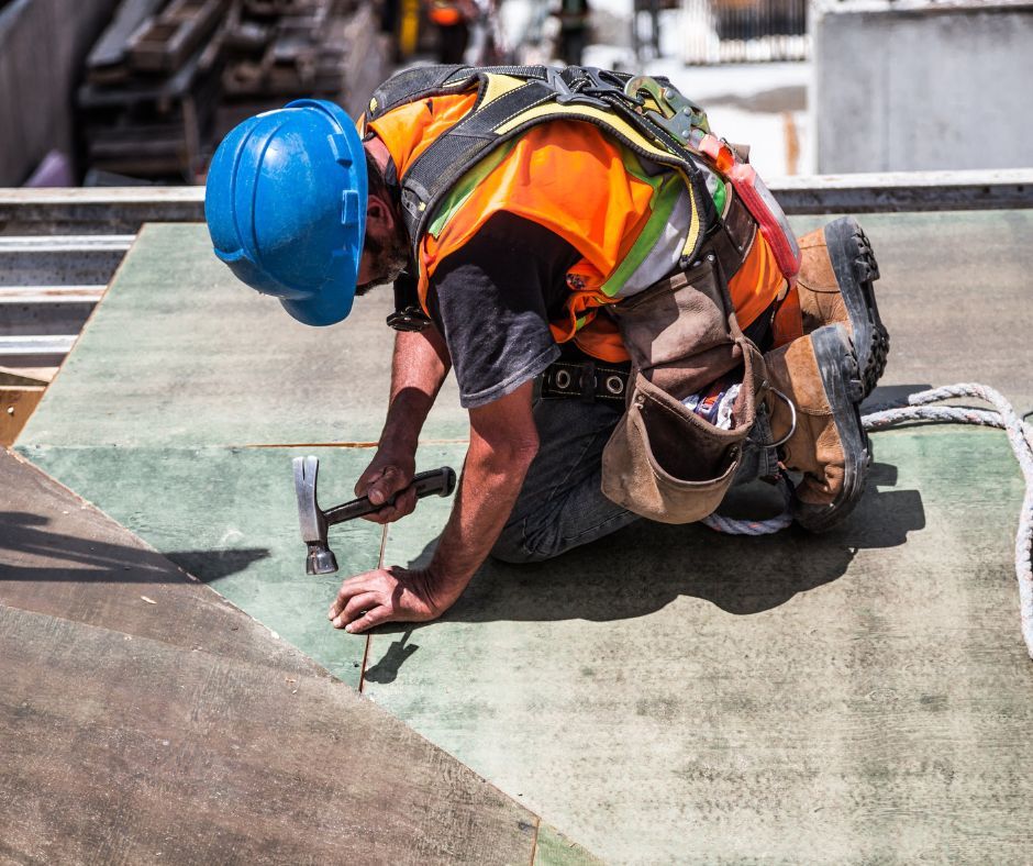 A construction worker is working on a roof with a hammer.
