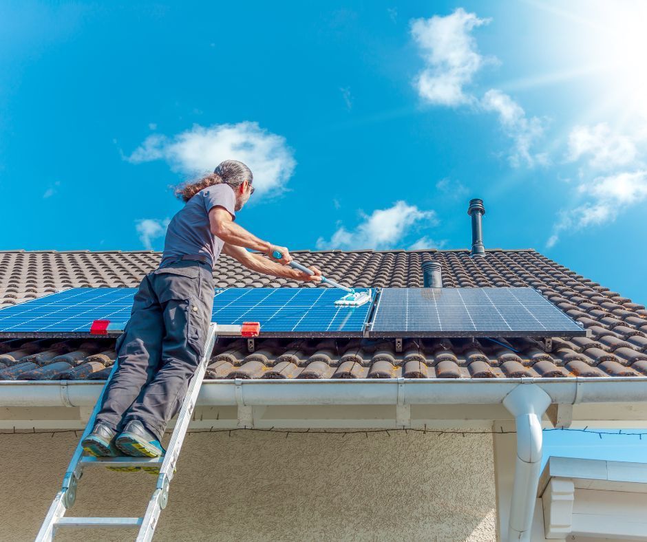 A man is standing on a ladder installing solar panels on the roof of a house.