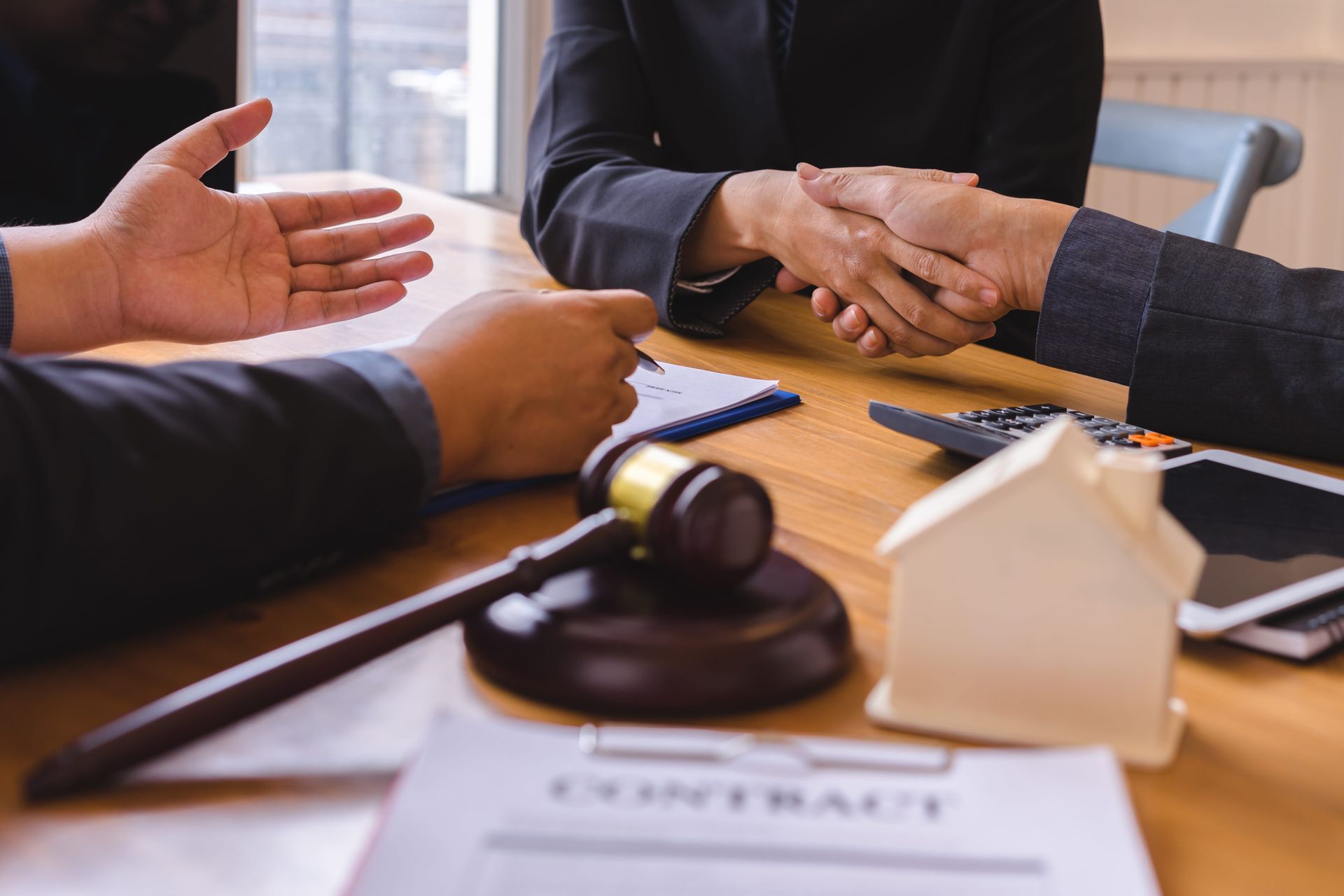 Hands shaking over a wooden table during a legal meeting, with a gavel and contract papers nearby