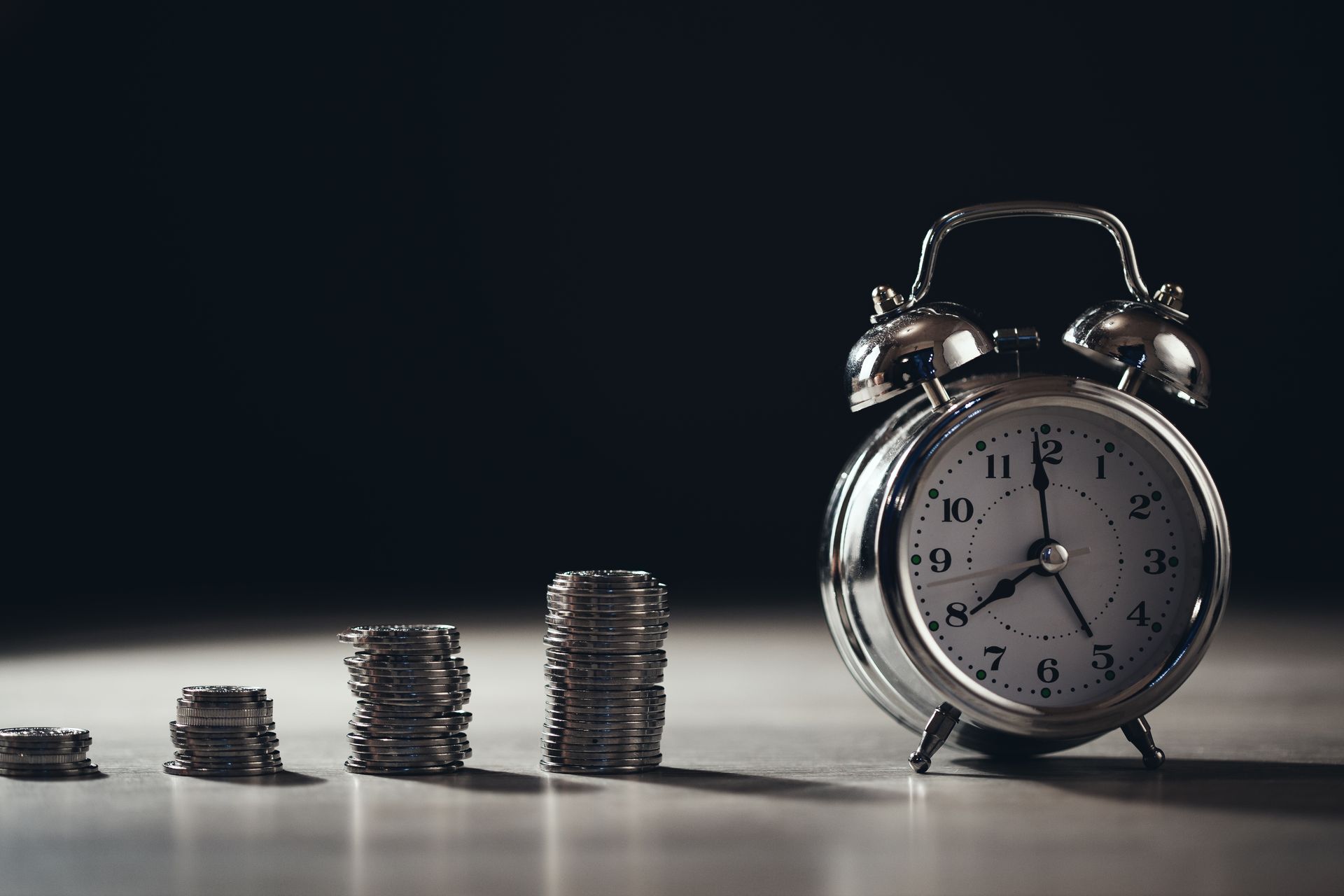 An alarm clock is sitting next to stacks of coins on a table.