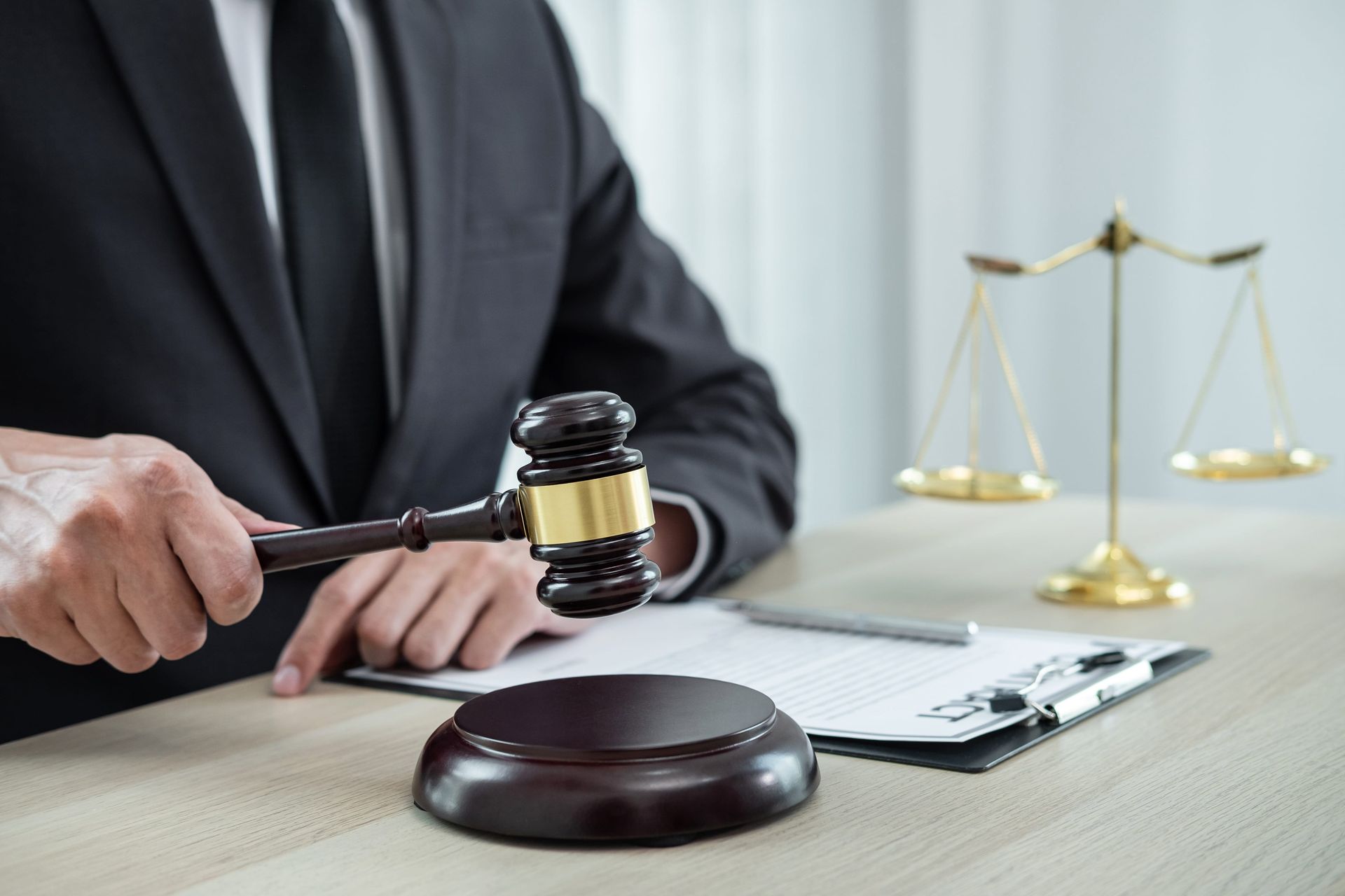 Lawyer in a suit striking a gavel beside a courthouse scale and paperwork on a desk