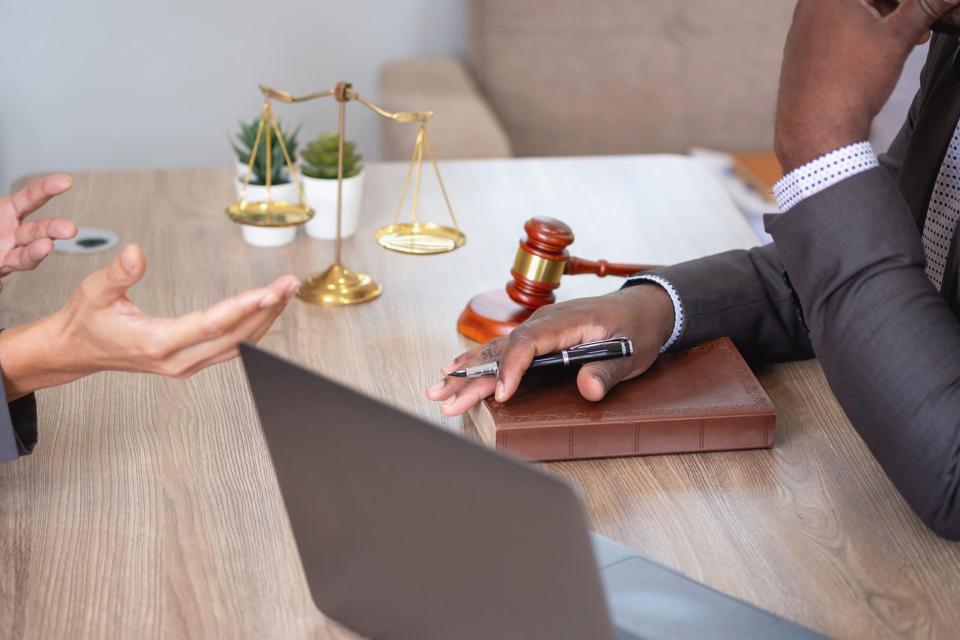 Lawyer discussing a case at a desk with scales of justice and gavel, laptop in foreground