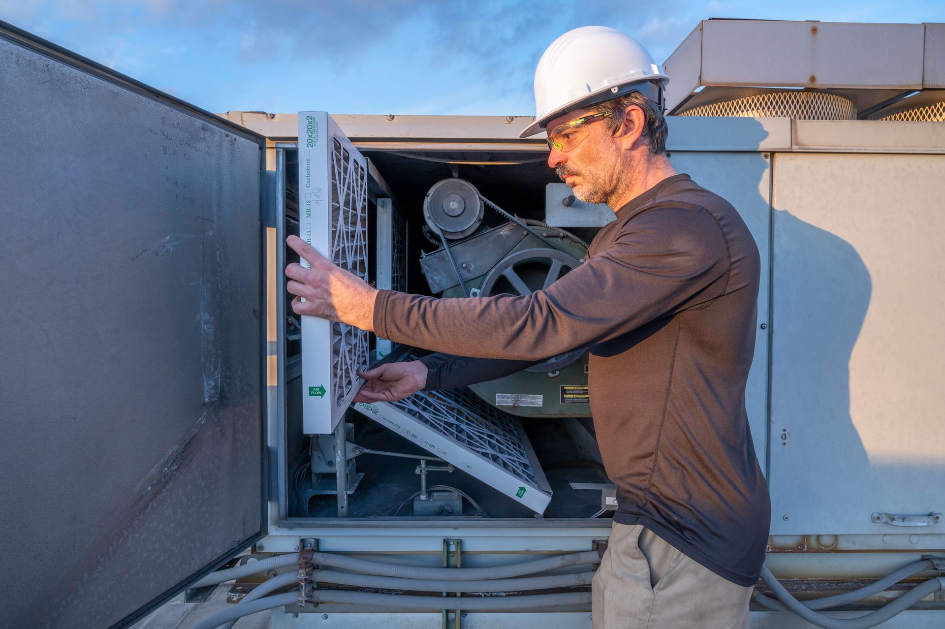 HVAC technician in a hard hat inspects air filters of an outdoor unit.