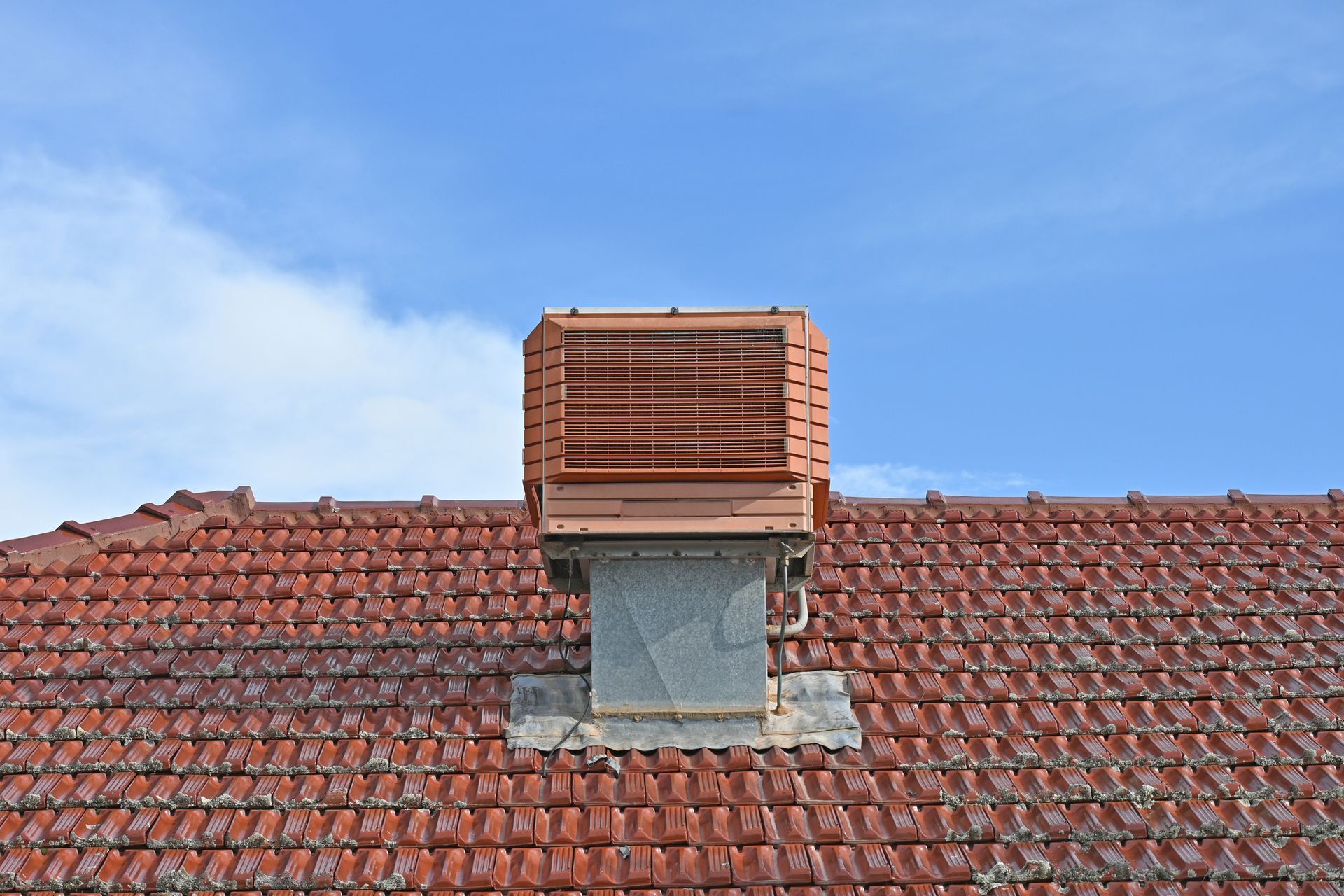 Rooftop with red tiles, a metal vent, and a brown exhaust fan against a blue sky.