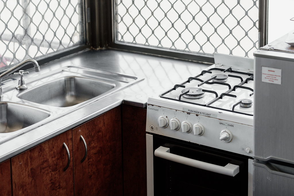 Kitchen corner with a sink, stovetop, and refrigerator. Brown cabinets, white appliances, and a window with security bars.