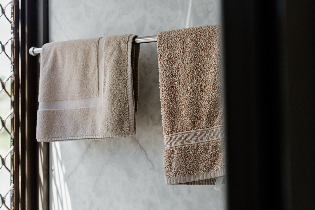 Two beige towels hanging on a silver towel rack against a marble wall.