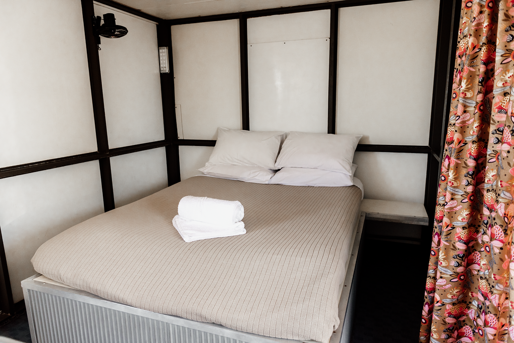 Bedroom with bed, pillows, folded towels, and patterned curtain.