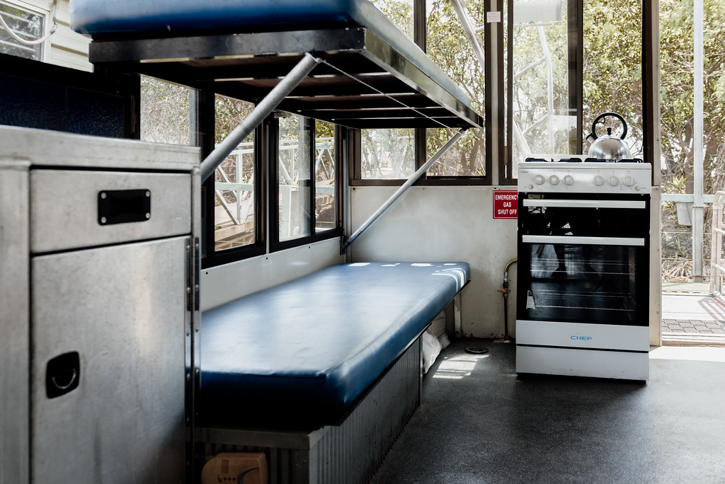 Bunk beds and a stove inside a room with windows; metal furniture, blue mattresses, white appliances.