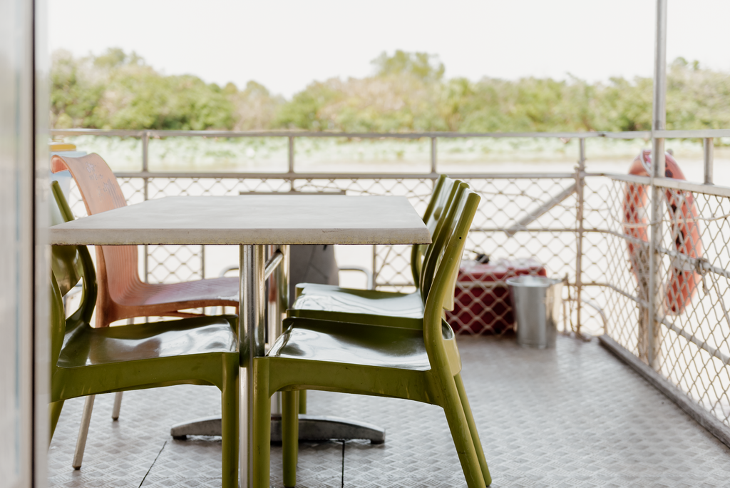 Table and chairs on a boat deck with a life preserver and scenic view.