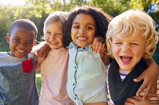 Four children smiling and hugging outdoors in bright sunlight