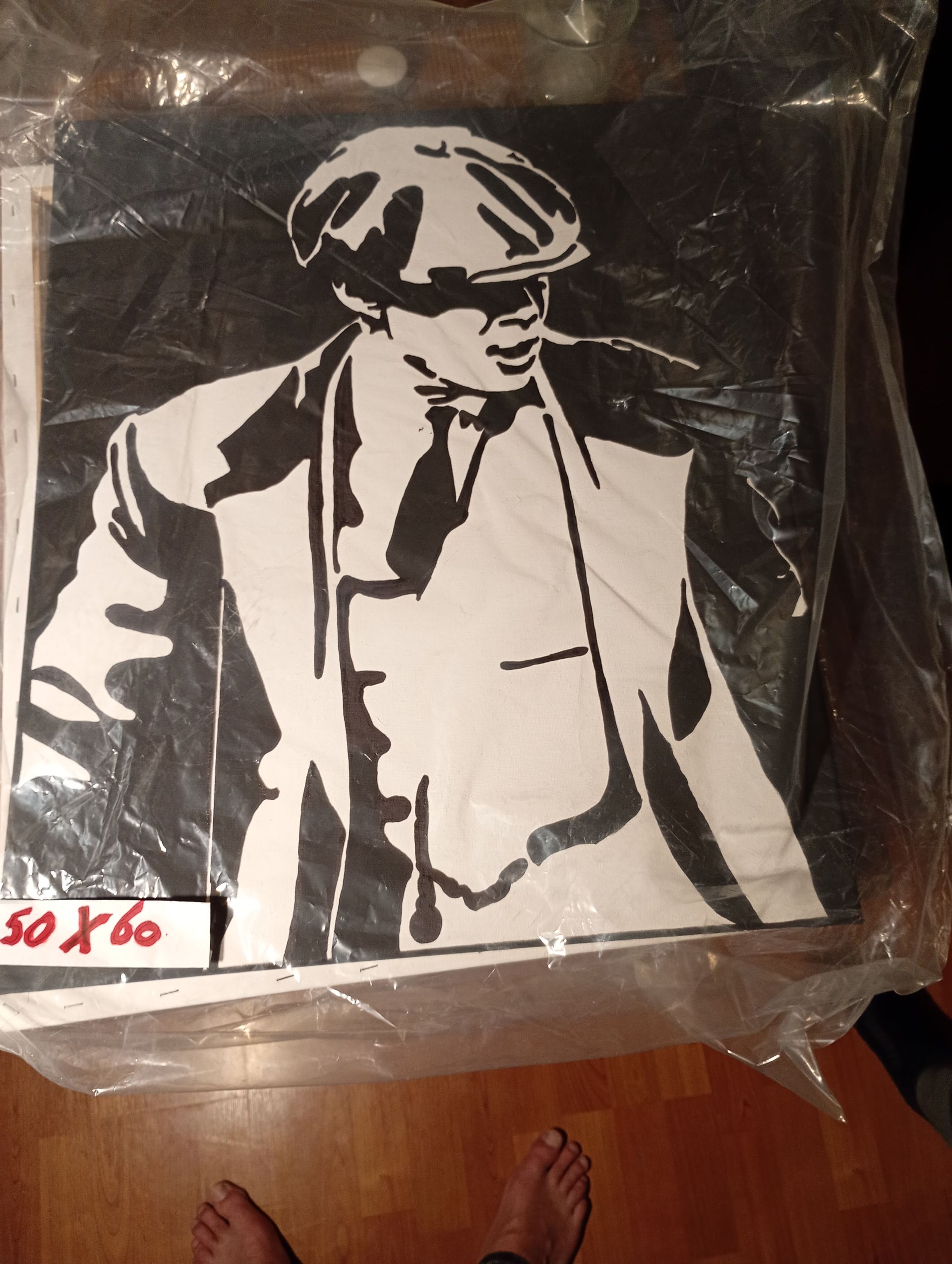 Zwart-witportret van een man in een pet en pak, een schilderij. In plastic verpakt, op een houten vloer.