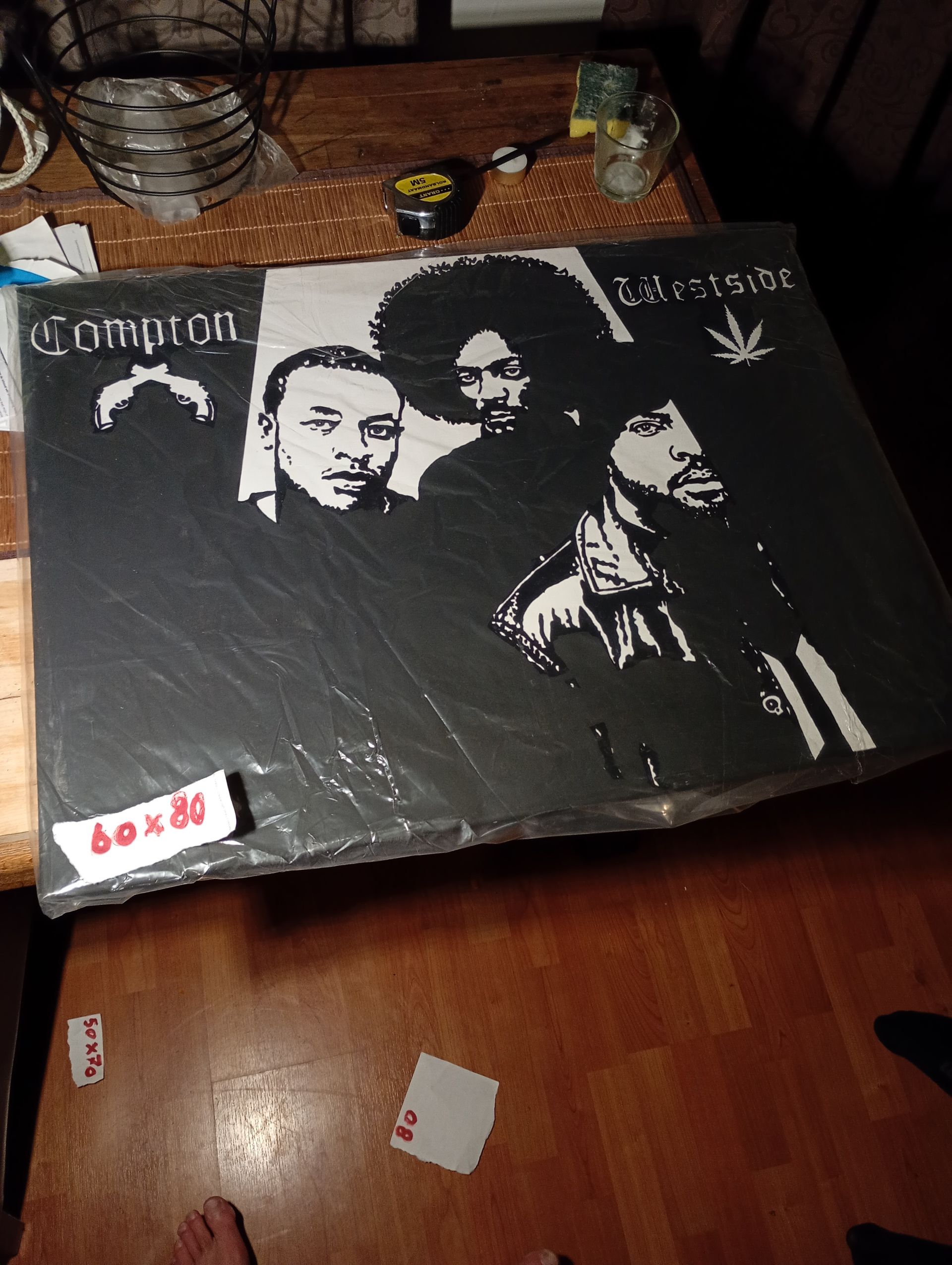 Zwart-witposter van drie mannen, Common en twee anderen, met een cannabisblad op een tafel.