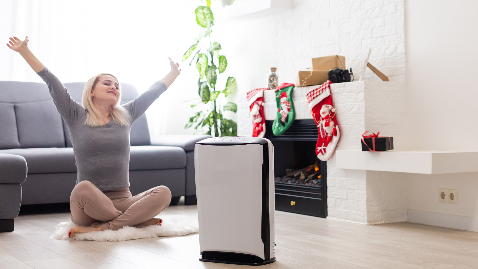 Air purifier in the living room with a woman, indoor plants, Christmas stockings, and a fireplace in the background.