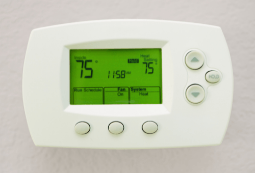 A white rectangular programmable thermostat showing 75 degrees Fahrenheit setting on its green-colored screen