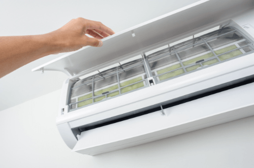 A person's hand is lifting the cover of a white air conditioner indoor unit, showing the newly cleaned filters