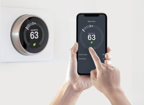 A person setting up a circular smart thermostat installed on a wall through a smartphone