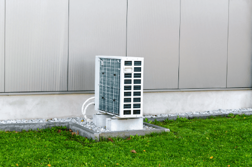 A commercial ductless heat pump installed on the grassy area near the gray exterior walls of a building