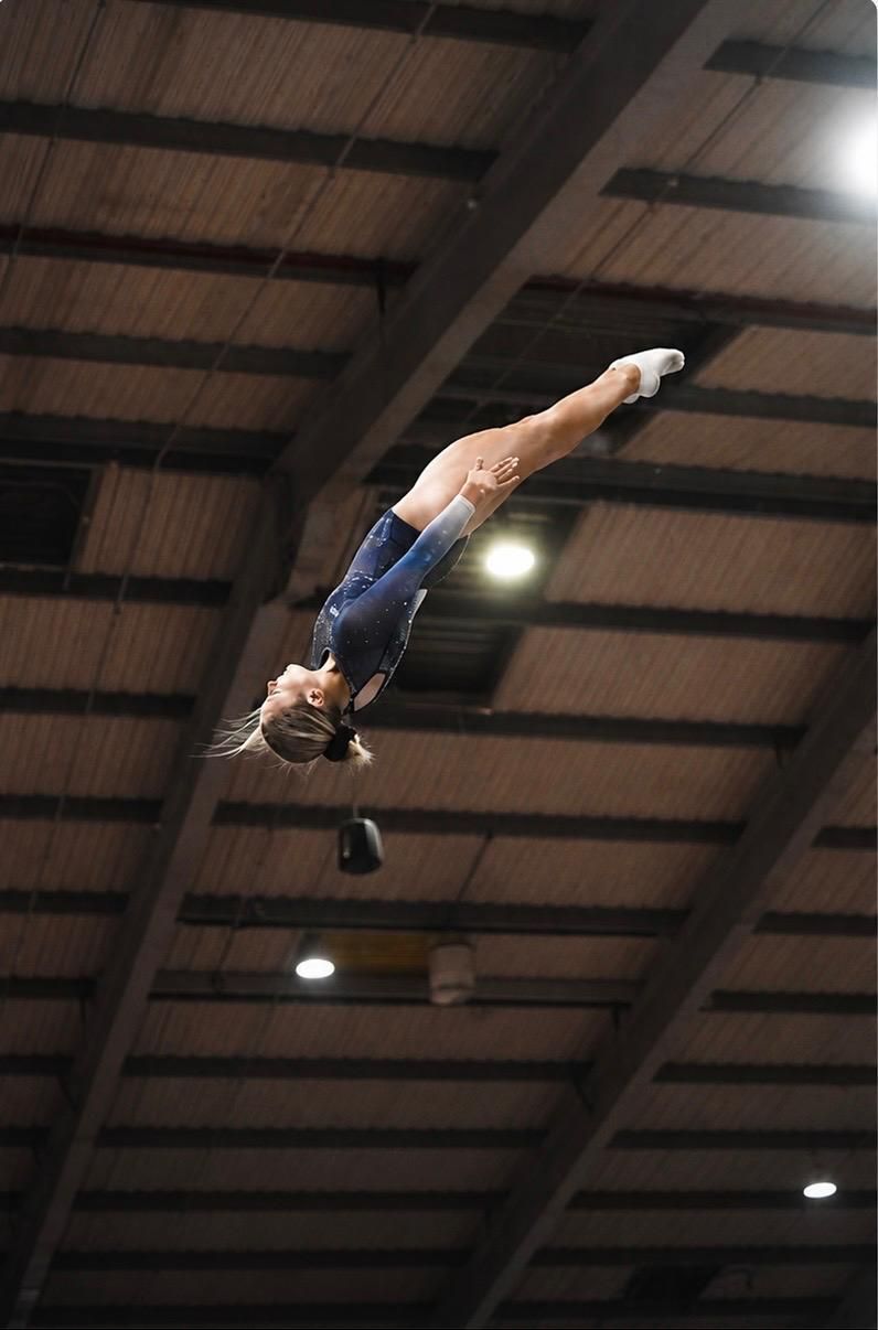 Gymnast mid-air performing a backward flip under a high indoor ceiling