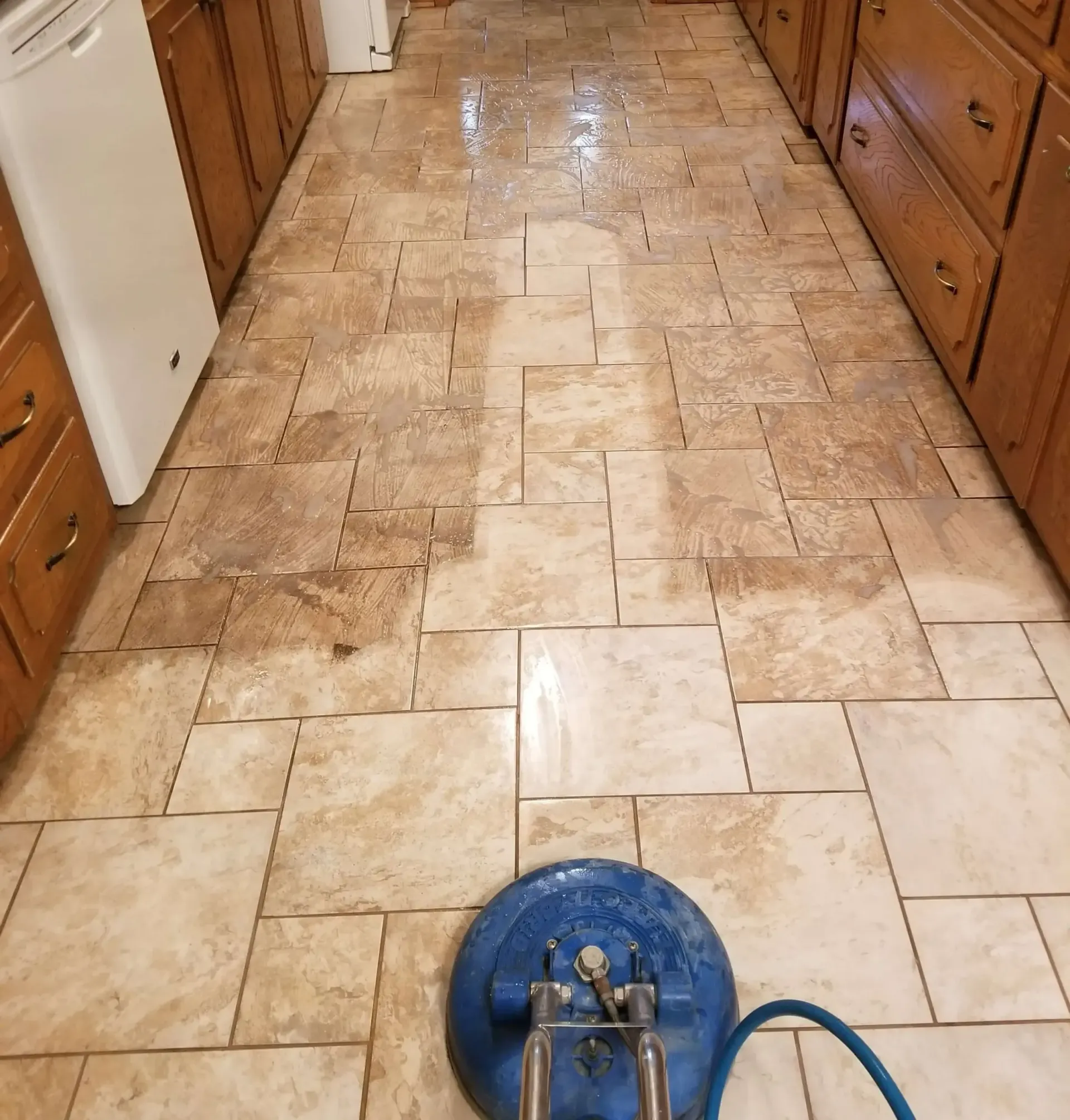 A blue vacuum cleaner is cleaning a tile floor in a kitchen