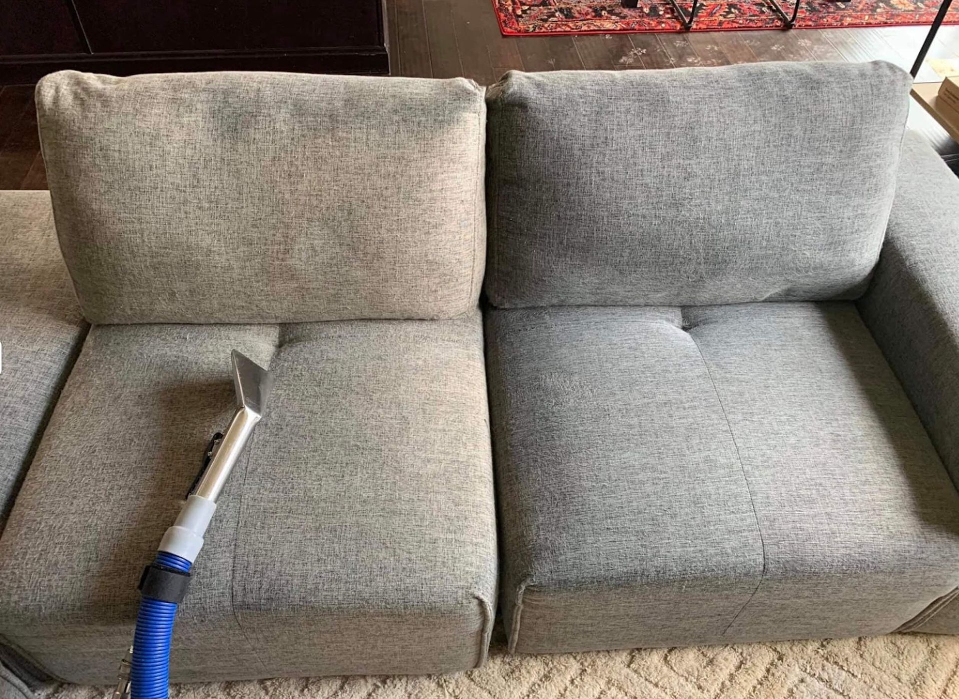 A couch is being cleaned with a vacuum cleaner in a living room.
