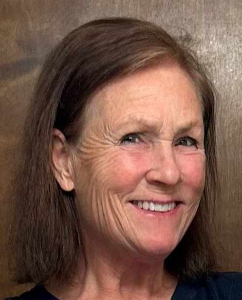 Woman with short brown hair smiles, posing in front of a wooden backdrop.