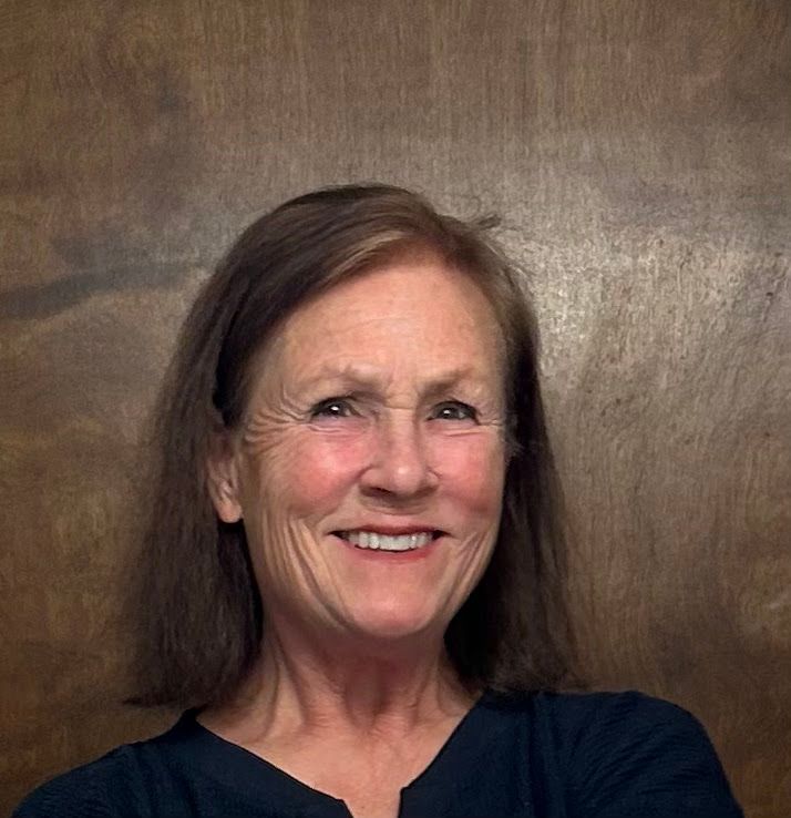 Woman with brown hair smiles, facing slightly right, against a neutral background.