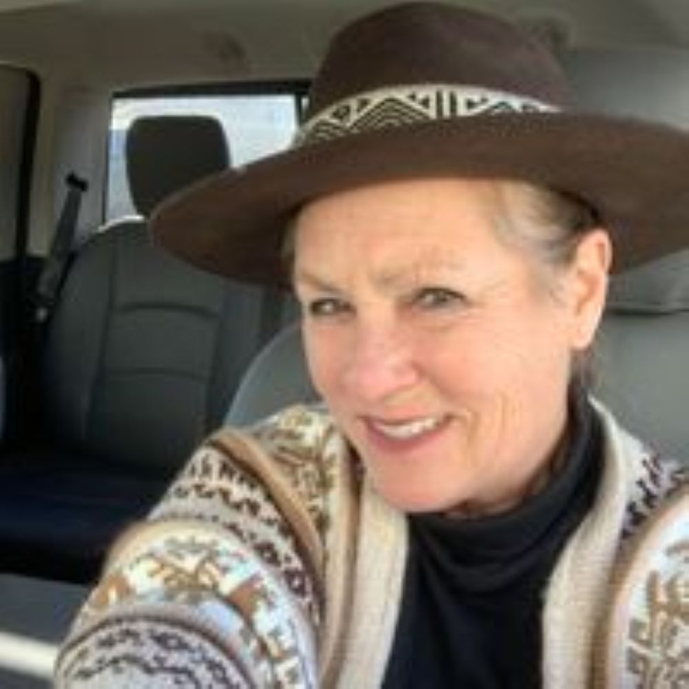 Woman in brown hat and patterned sweater smiles in a car.