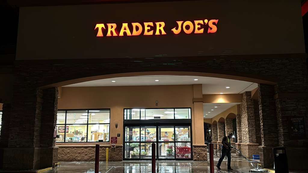 An exterior view of a Trader Joe's grocery store at night, featuring a stone-facade entrance and glowing sign.