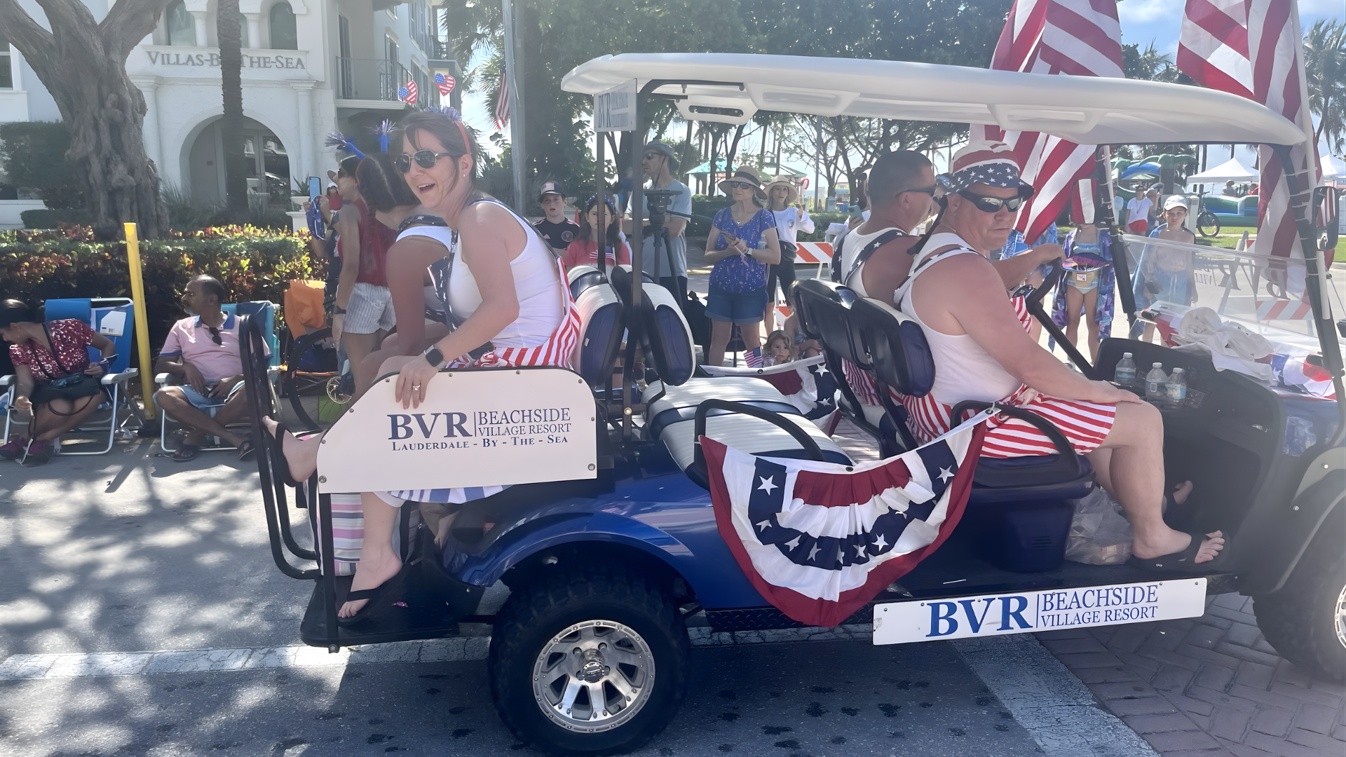 People in patriotic outfits on a decorated golf cart in a parade.