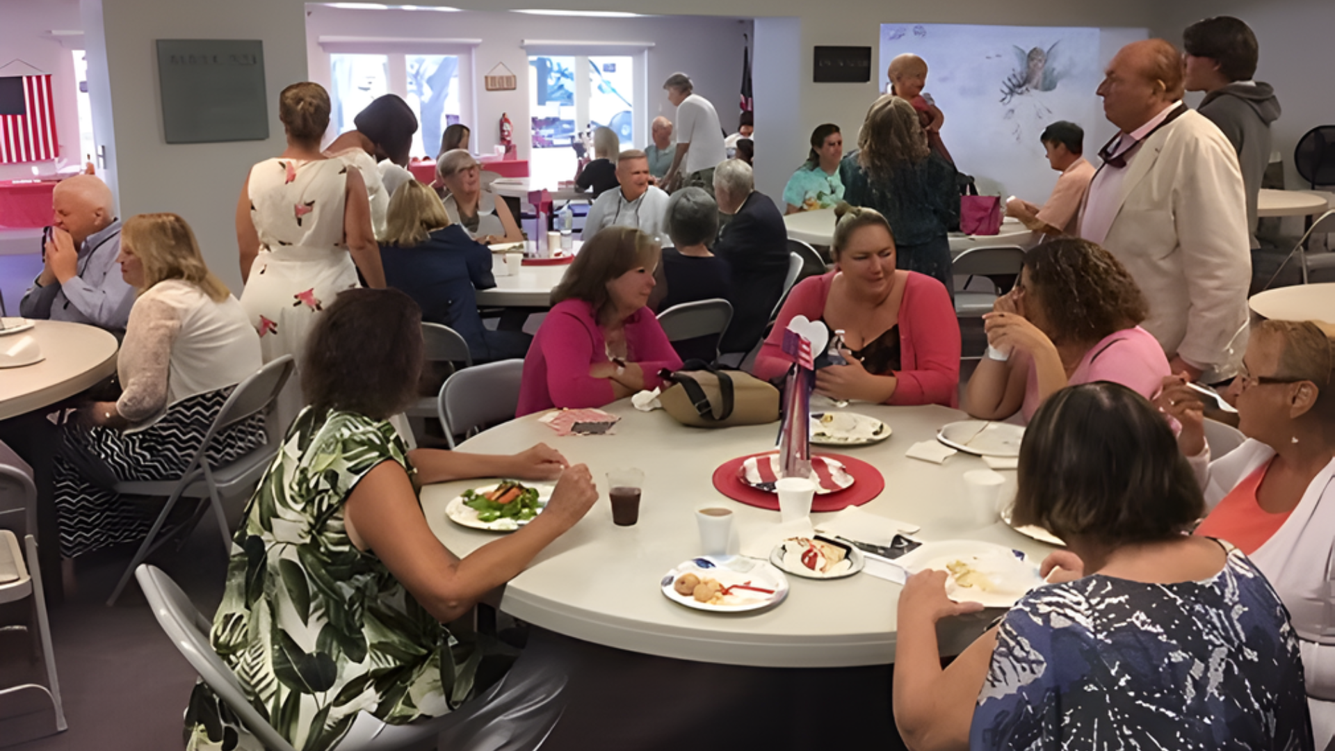 People gathered at round tables in a community room for an event, some eating and talking.