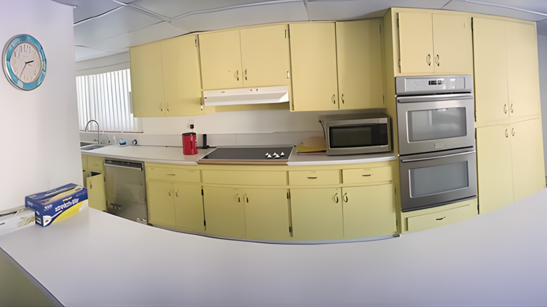Kitchen with light yellow cabinets, stainless steel appliances, and a round clock on the wall.