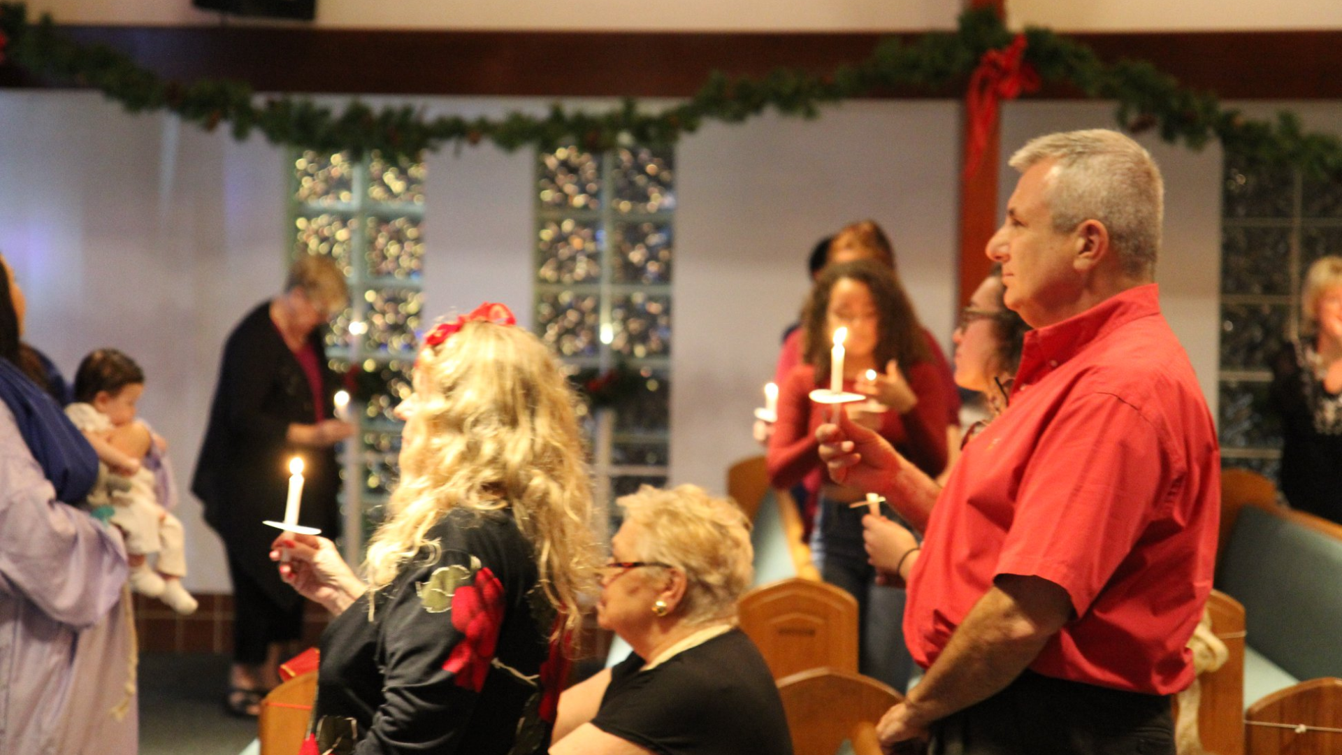 People holding lit candles during an event indoors, possibly a church service with festive decorations.