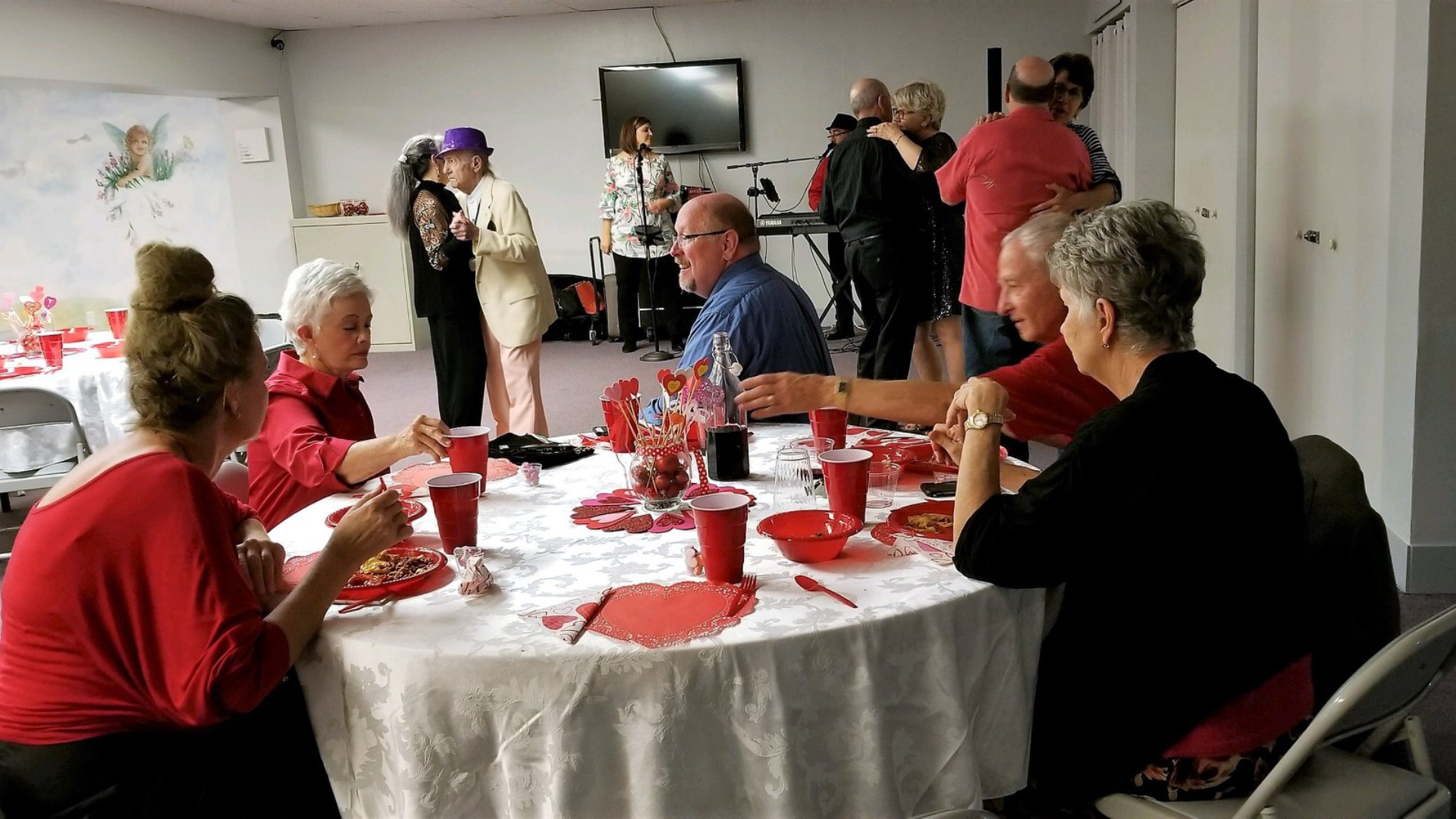 People at a party, eating and dancing. Red and white decorations. A band plays.