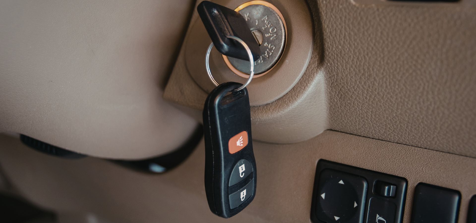 A car key with a remote fob inserted into the ignition switch of a vehicle's dashboard.
